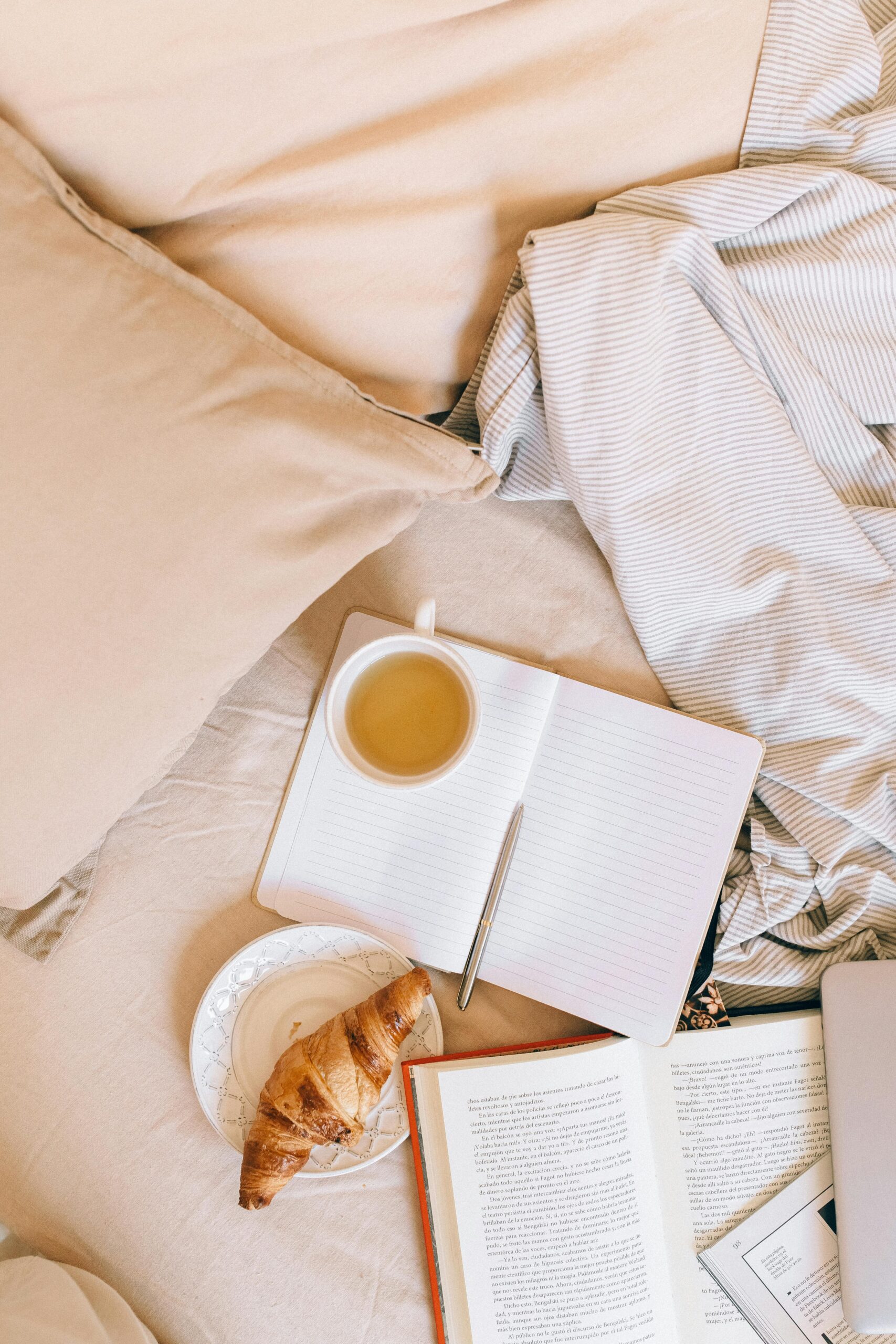 Top view of a cozy bed with tea, croissant, and open notebook, ideal for relaxation themes.