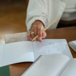 Close-up of a person writing in a graph notebook with a pencil at a wooden table, ideal for study and education themes.